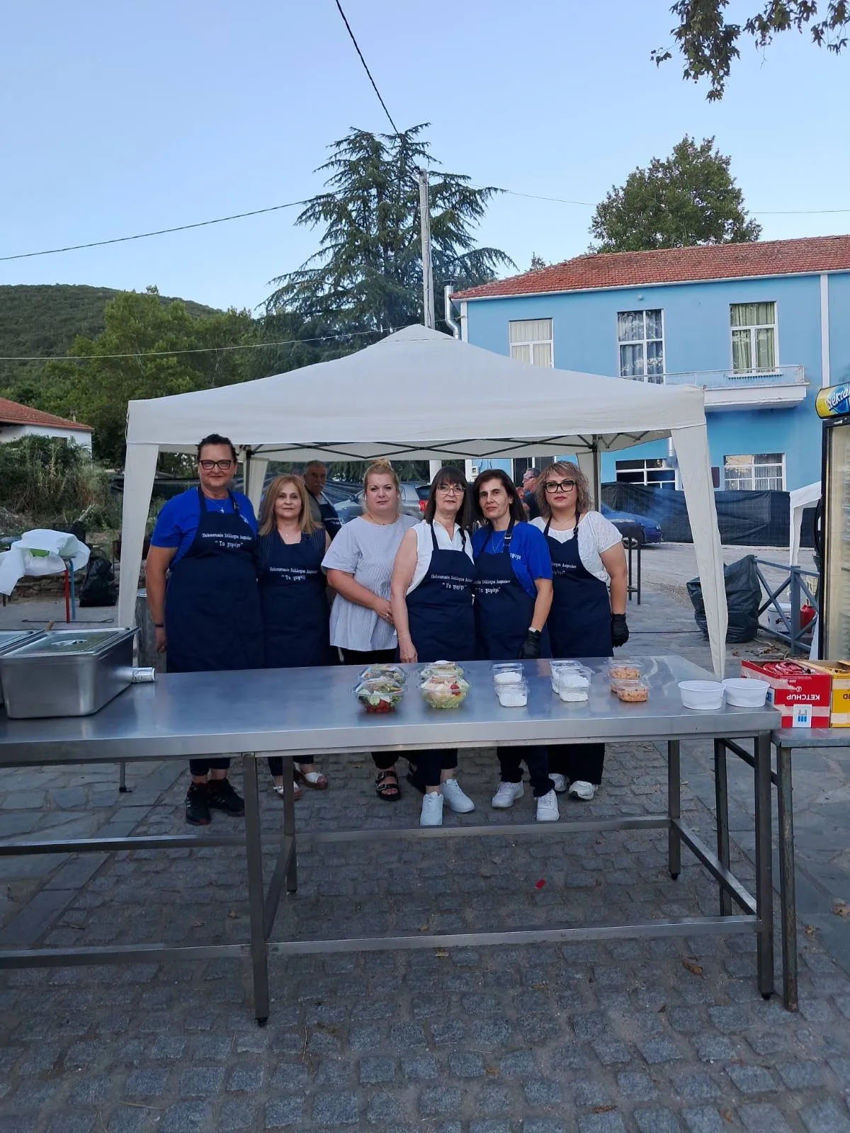 Οι εθελόντριες του συλλόγου με τις ποδιές «Το Γεφύρι» στον πάγκο του φαγητού